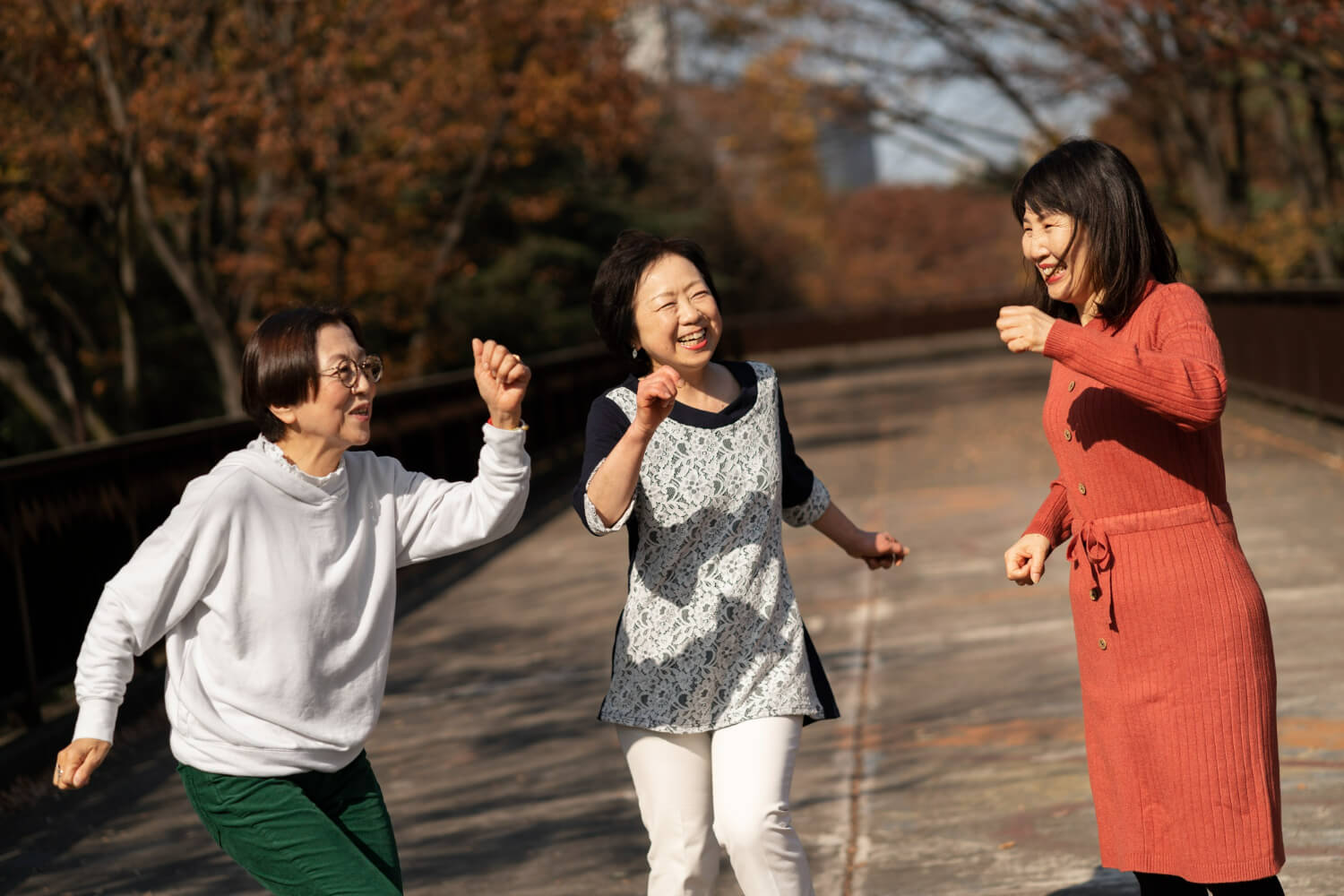 세 명의 중년과 노인 여성이 도로 위에서 팔을 흔들며 즐거워 하고 있다.