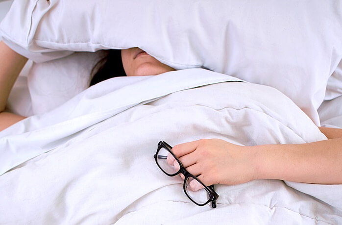 침대 위에 누워있는 여자가 베개로 얼굴을 가리고 있다.