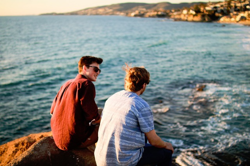 바닷가 바위 위에 앉아 마주보고 웃고 있는 남성 두명 친구