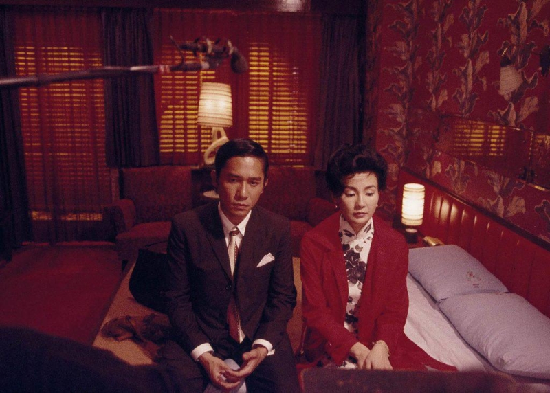 차우와 첸 부인이 정면을 응시하며 나란히 침대에 걸터 앉아 있는 모습