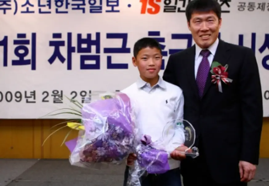 흰플랭카드 1회 차범근 축구시상 글자 앞 보라색 꽃다발을 들고 있는 황희찬과 그옆 검은양복을 입은 차범근