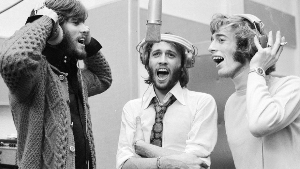 서로를 바라보며 한 개의 마이크 주위에서 함께 노래를 부르는 형제들 Bee Gees