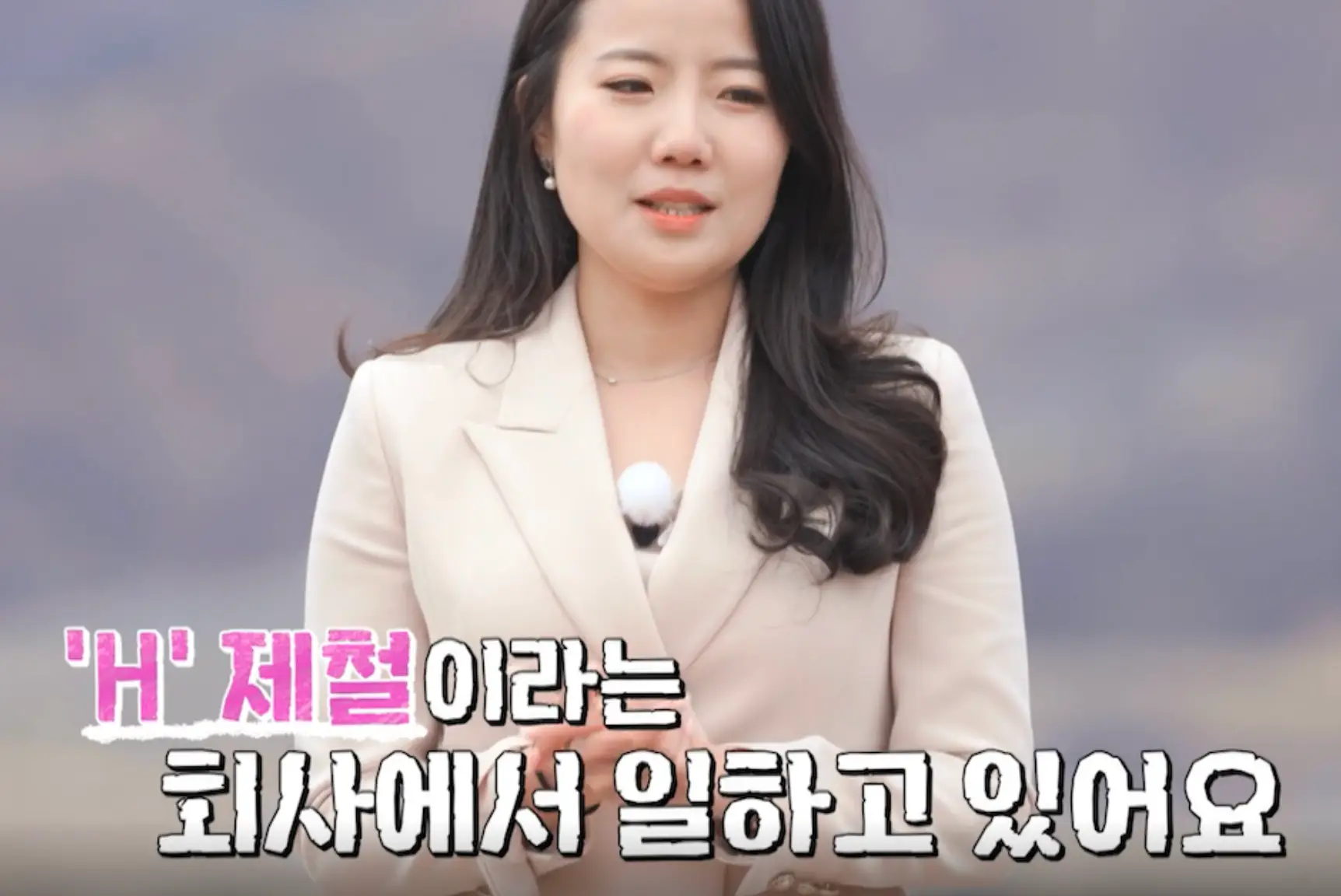 나는솔로-야산배경 흰정장입여자가 긴머리를 늘어뜨린채 말하는 모습 아래 분홍글싸&amp;#39;H&amp;#39;제철이라는 회사에서 일하고 있어요