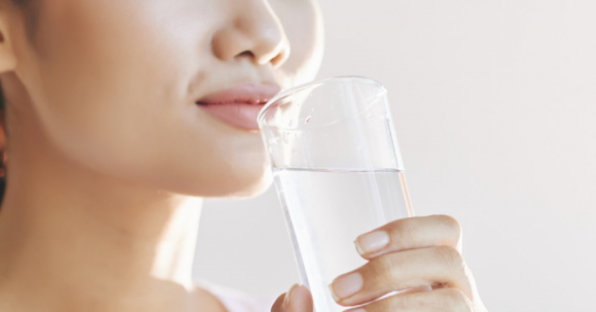 손으로 투명한 컵을 들고 물을 마시려고 하는 여성의 사진