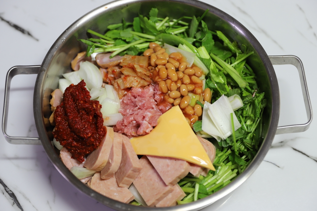 냄비에 부대찌개 재료(햄, 김치, 돼지고기, 미나리, 양파, 양념장, 치즈) 모두 올린 사진