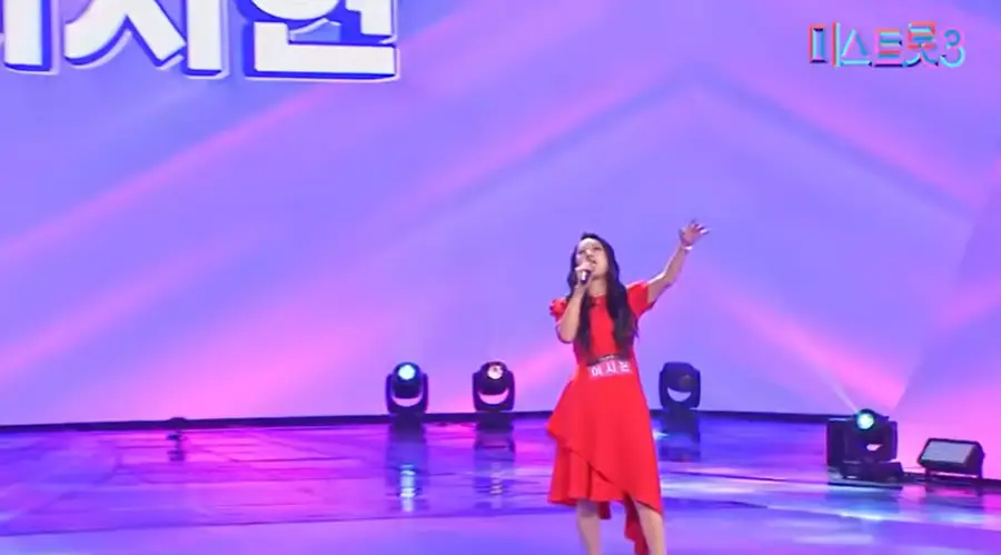 미스트롯3- 불은색 반팔 원피스를 입은 전신이 나온 모습으로 오른손으로 마이크를 든채 관중을 바라보고 노래하는 이시현 출연자