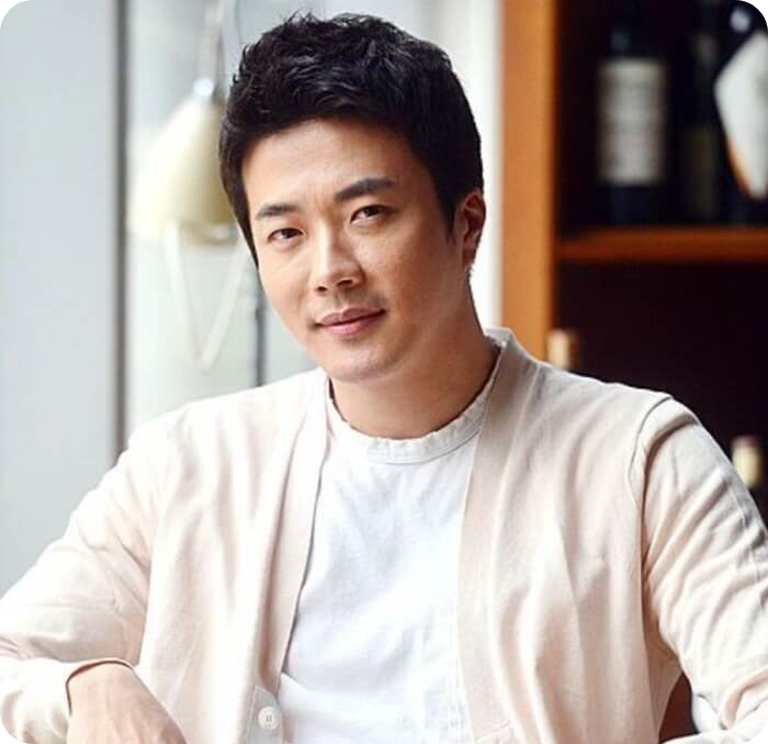 흰 티에 가디건을 입고 있는 배우 권상우의 모습. 앉아서 살짝 미소를 띄고 있다.