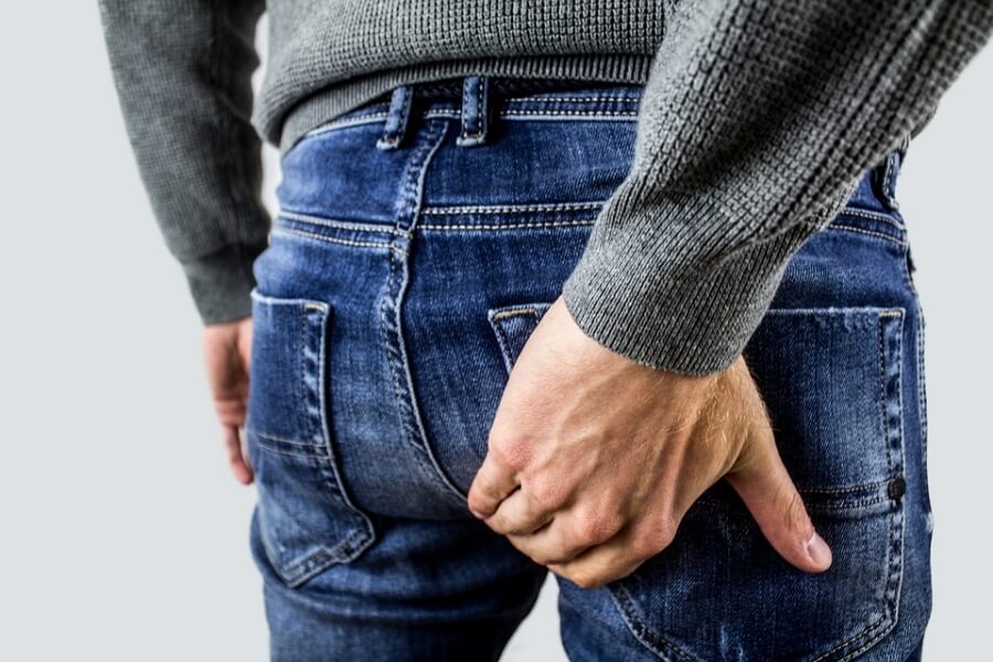 치핵의 통증으로 엉덩이에 손을 대고 있는 한 남자 사진