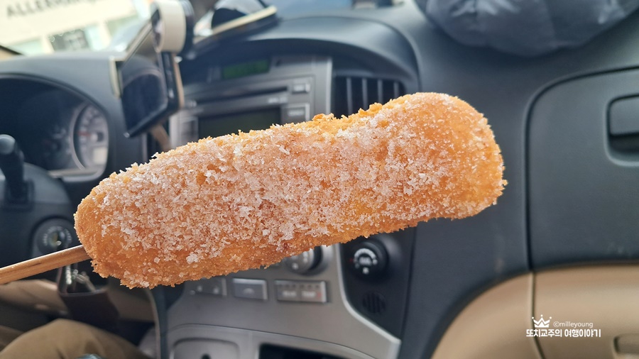 차 안에서 설탕에 묻힌 핫도그를 손에 들고 있다