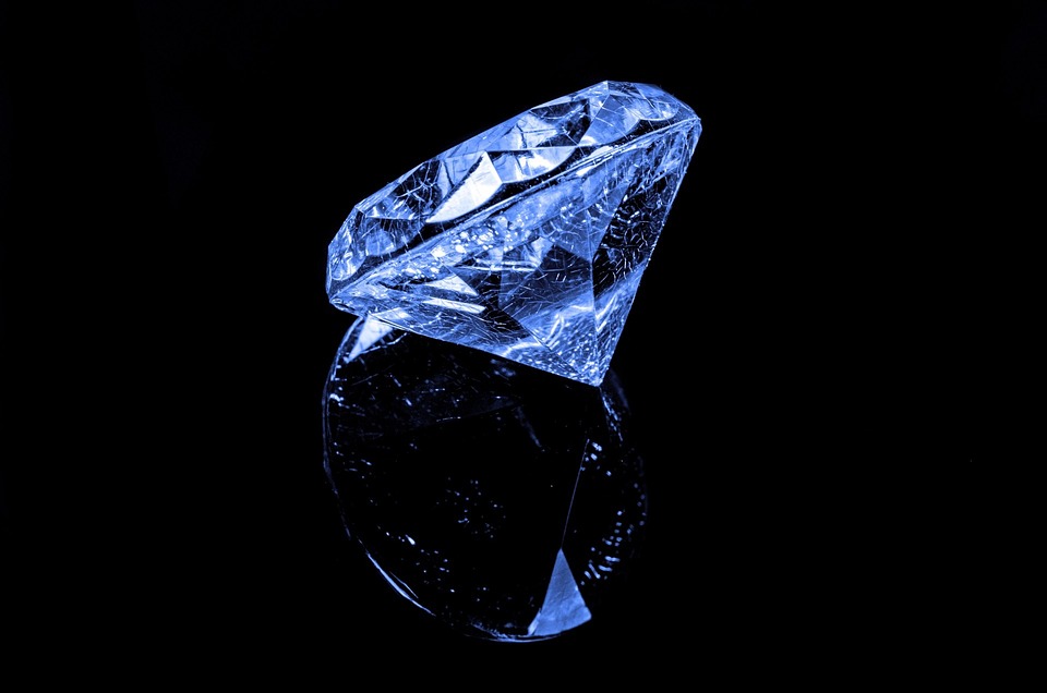 검은 배경의 유리 위에 푸른 빛의 다이아몬드가 반사되어 보이는 사진입니다. 다이아몬드 안쪽에 내포물이 그대로 보입니다. 내포물은 다이아몬드가 고온과 고압을 견뎌낸 흔적입니다. 수분과&#44; 탄소를 제외한 다른 물질들이 타들어 가면서 남긴 흔적입니다.