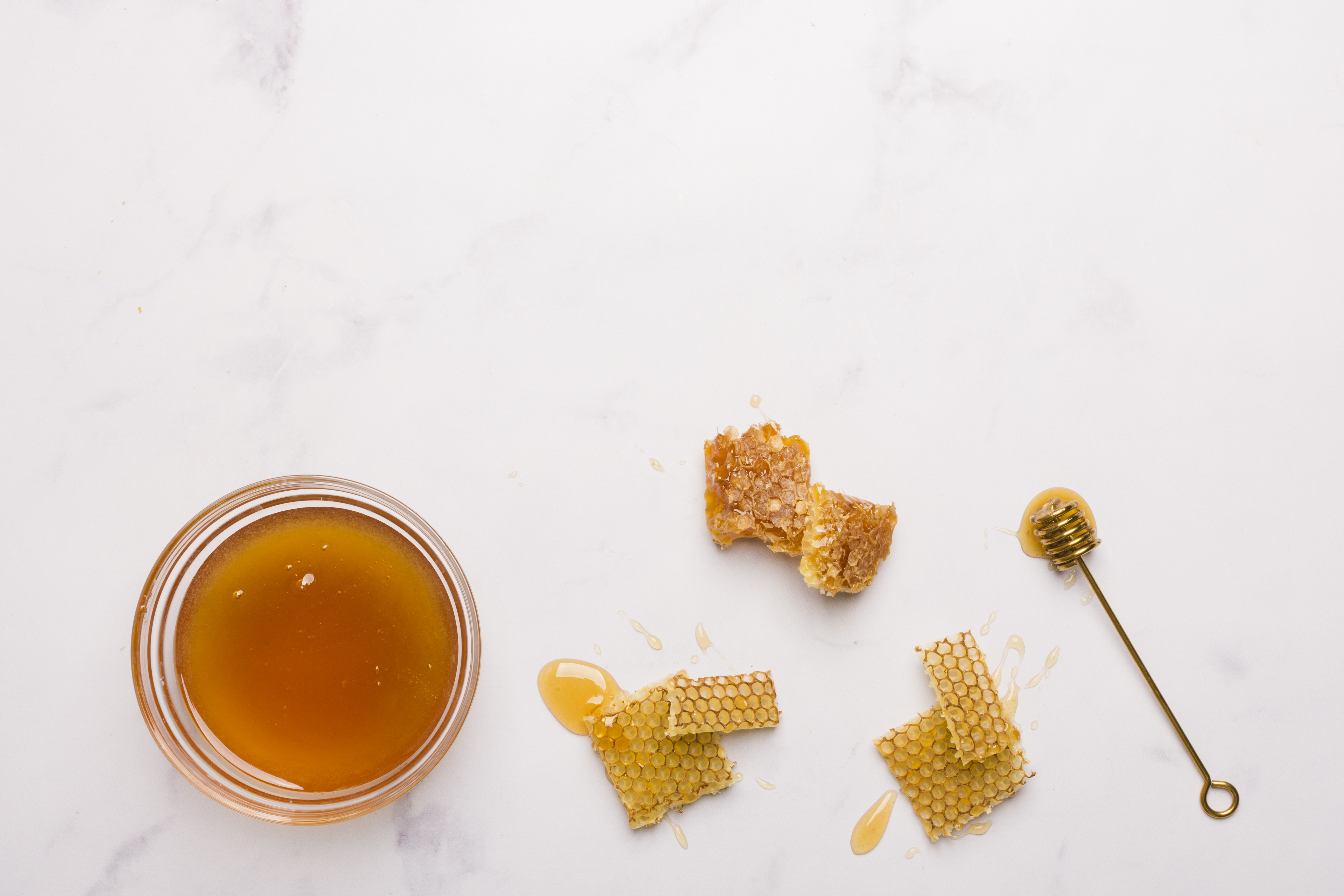top-view-honey-with-honeycomb-pieces 하얀 바닥에 꿀을 가득 담아 놓은 꿀통을 뚜껑을 열어 놓은 상태로 두었고, 그 옆에는 꿀이 묻어 있는 벌집 조각을 두었고, 그 옆에는 꿀이 묻어 있는 숟가락을 둔 사진