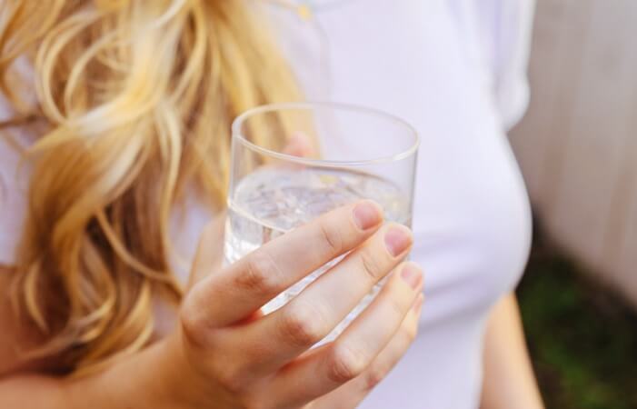 하얀 티셔츠를 입은 금발의 여자가 손에 물 컵을 쥐고 있는 모습
