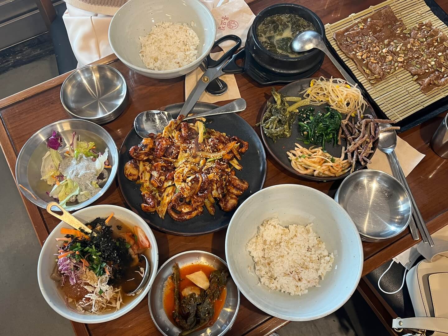 테이블 위에 쭈꾸미 한상 음식 사진 (쭈꾸미&#44; 나물 5가지&#44; 도토리전&#44; 샐러드&#44; 묵사발&#44; 김치&#44; 공기밥이 한상 가득 놓여있음)