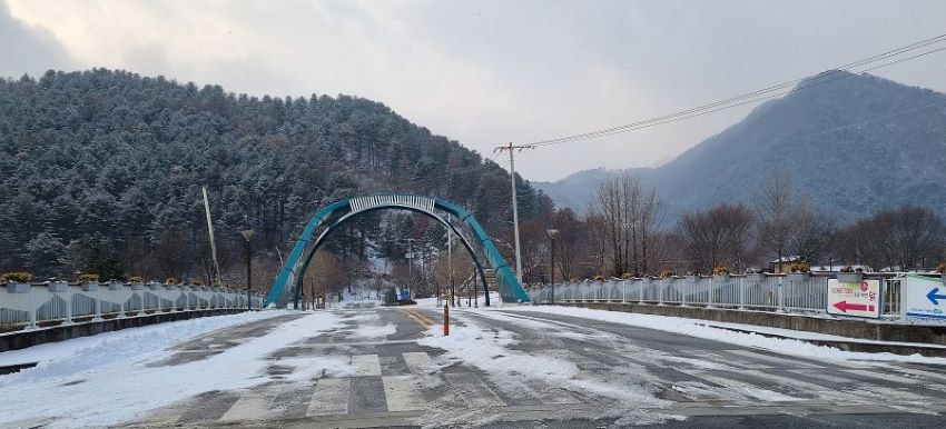 흐린 하늘, 야산, 다리 위에 아치형 구조물, 푸른색, 양 옆으로 교량 안전난간,