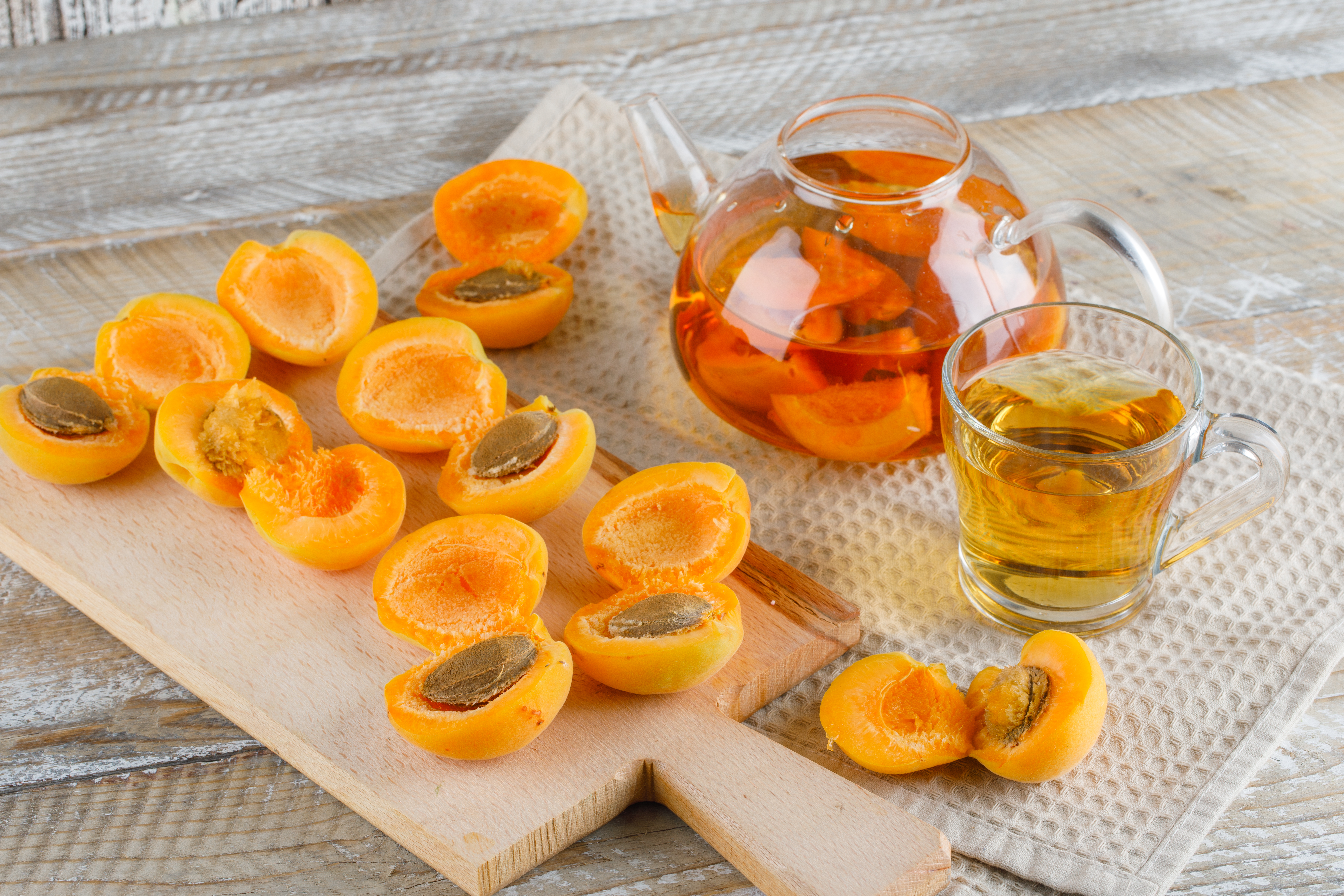 apricot-tea-teapot-mug-with-apricots-cutting-board-top-view-wooden-kitchen-towel