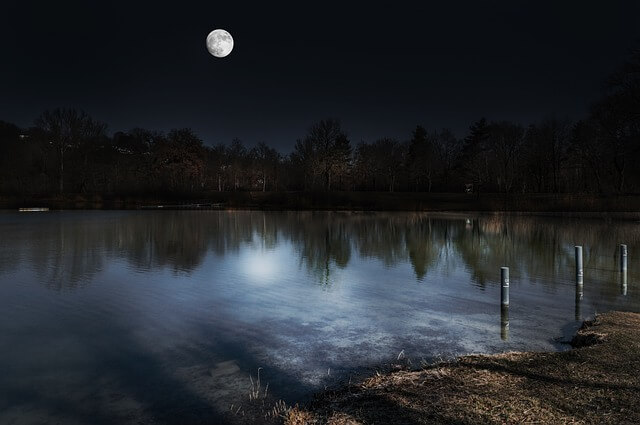 어두운 밤에 호수 위에 달이 떠있다.