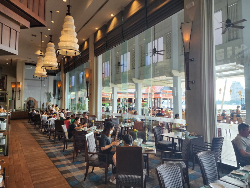 아난타라 리버사이드 조식 식당의 실내 모습. 매우 높은 천장에 태국 전통스러운 큰 등이 연이어 3 개가 달려 있고 밑에는 식사 테이블이 있는데 사람들이 테이블을 가득 메우고 있다.