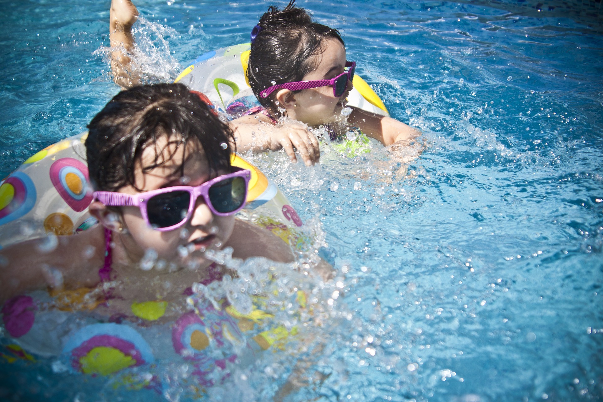 두 명의 어린 아이가 선글라스를 끼고 튜브에 몸을 기대어 수영하고 있다