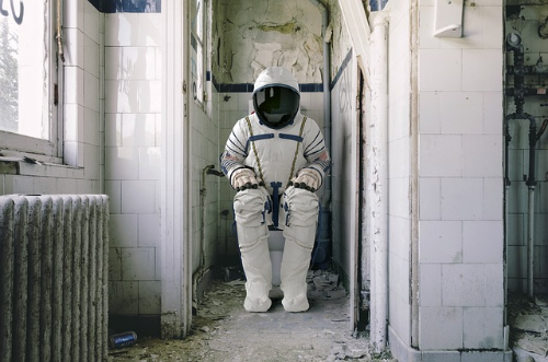 우주복을 입은 사람이 화장실 변기에 앉아있는 사진
