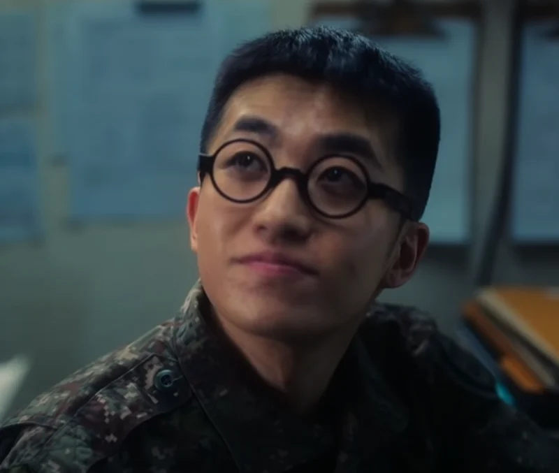 군 사무실을 배경으로 군복을 입고 뿔테 안경을 쓴 DP 시즌 2의 허기영