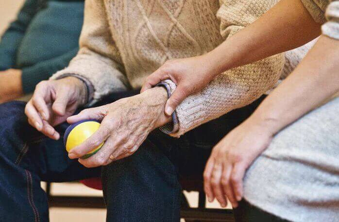 노란색의 작은 공을 손에 쥐고 있는 노인의 팔목을 잡고 있는 한 여자