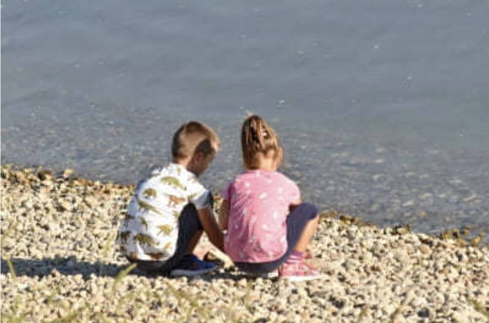 바다 앞에서 어린 남매가 앉아서 놀고 있다