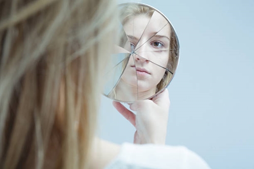깨진 거울로 자신을 보고 있는 여자의 모습 사진