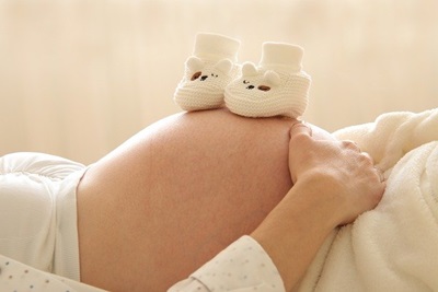 임신한-여성이-누워서-배위에-아기-신발을-올려놓고있는-장면