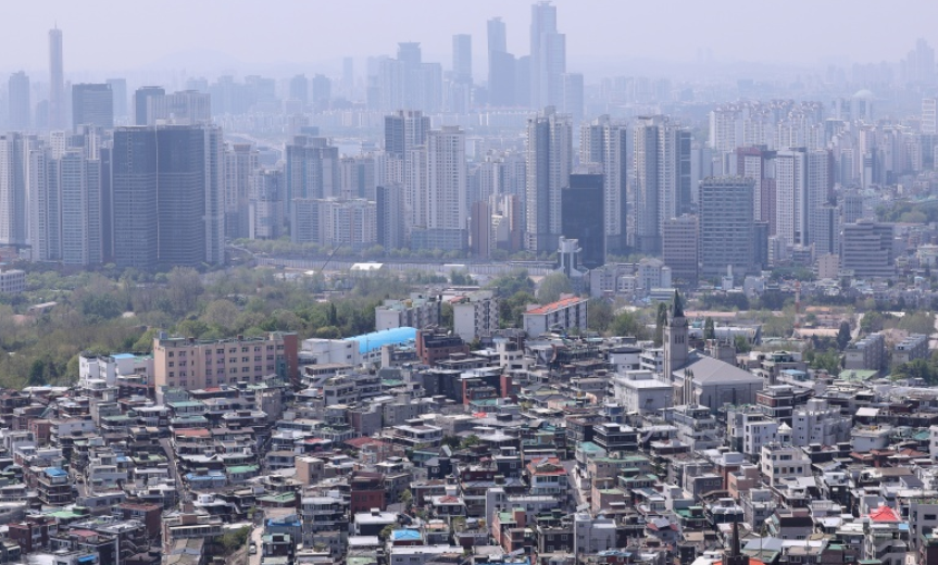서울 도심의 전경을 담은 사진으로, 앞쪽에는 저층 빌라와 연립주택들이 밀집해 있고, 뒤편으로는 고층 아파트와 초고층 빌딩들이 빽빽이 들어선 모습. 도시의 양극화된 주거 형태가 대비되며, 흐릿한 미세먼지 속에 서울의 스카이라인이 뚜렷하게 보인다.