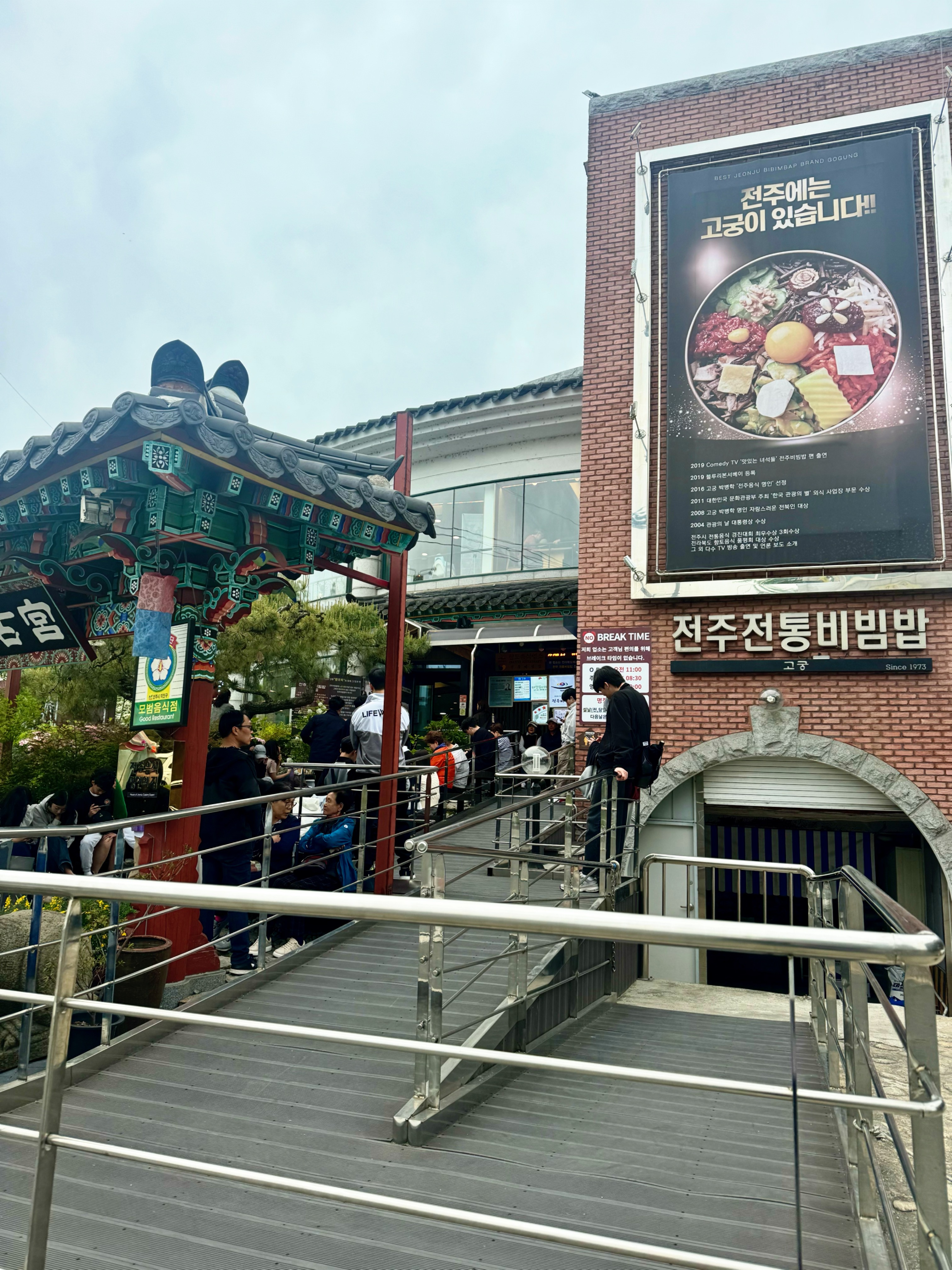 전주 고궁비빔밥 본점 입구와 기다리는 손님들. 전통 건축 양식의 정자와 고궁 간판이 함께 보이며, 붐비는 대기줄에서 맛집의 인기를 실감할 수 있다.