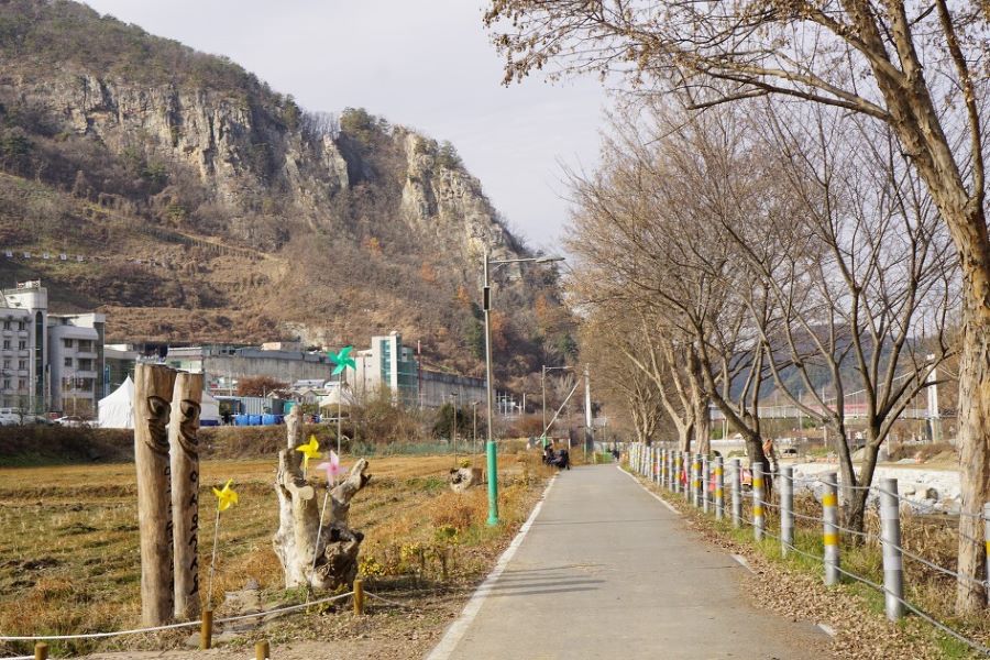 강촌역으로 가는 길&#44; 빼곡한 가로수&#44; 뒤로 왼편에 바위절벽&#44; 회색하늘&#44;