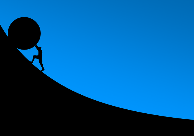 남성이 가파른 언덕에 커다란 둥근물체를 힘을 내어 밀어붙이며 올라가는 사진