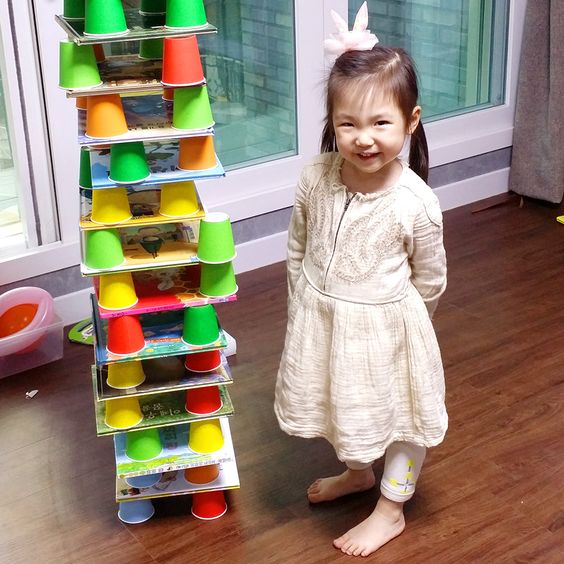 책과 책 사이에 종이컵을 엎어 두고 다시 책을 쌓는 과정을 반복하며 흐믓해하고 있는 여자아이