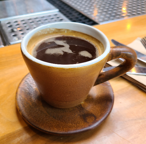 갈색 커피 잔에 커피가 담겨 있다. 컵 받침도 같은 색이다. 
