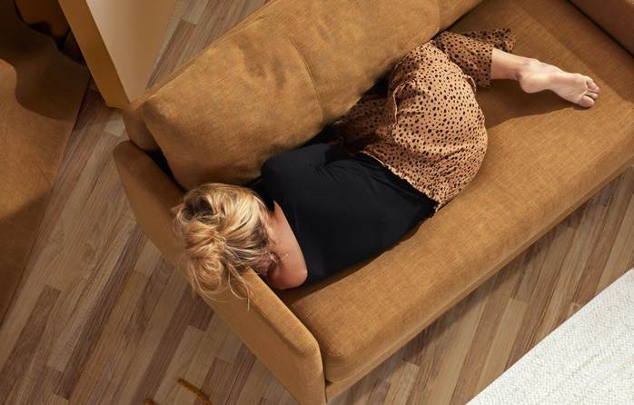 금발의 한 여자가 갈색의 패브릭 소파 위에 엎드려 자고 있는 모습