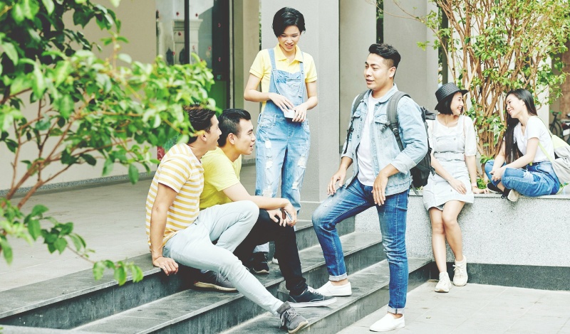 Group of students casually talking and smiling on campus steps near a school building