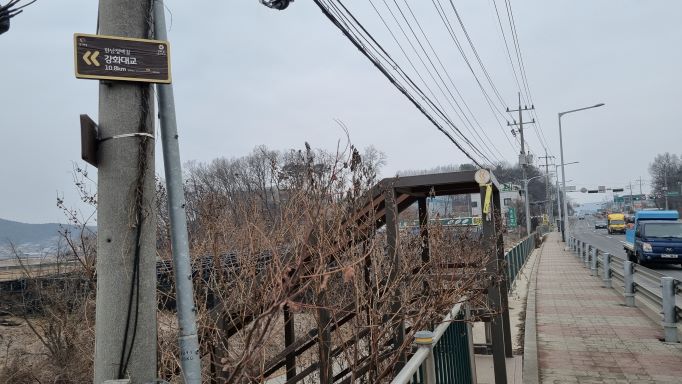 전봇대에 붙은 이정표&#44; 수많은 가닥의 전깃줄&#44; 우측에는 질주하는 차량들&#44; 왼쪽으로 내려가는 계단