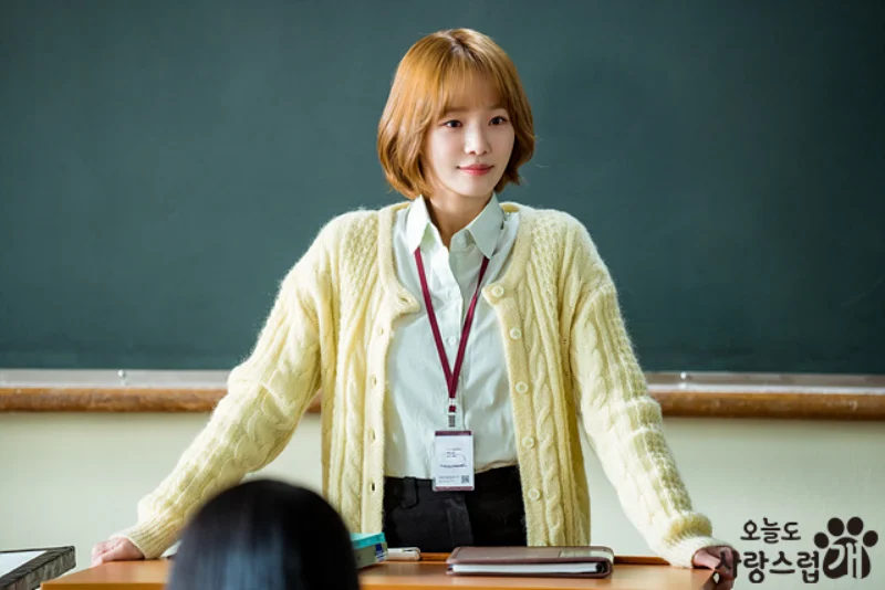 칠판을 배경으로 교실 교탁에 서 있는 갈색 단발 머리의 오늘도 사랑스럽개 출연 배우 박규영