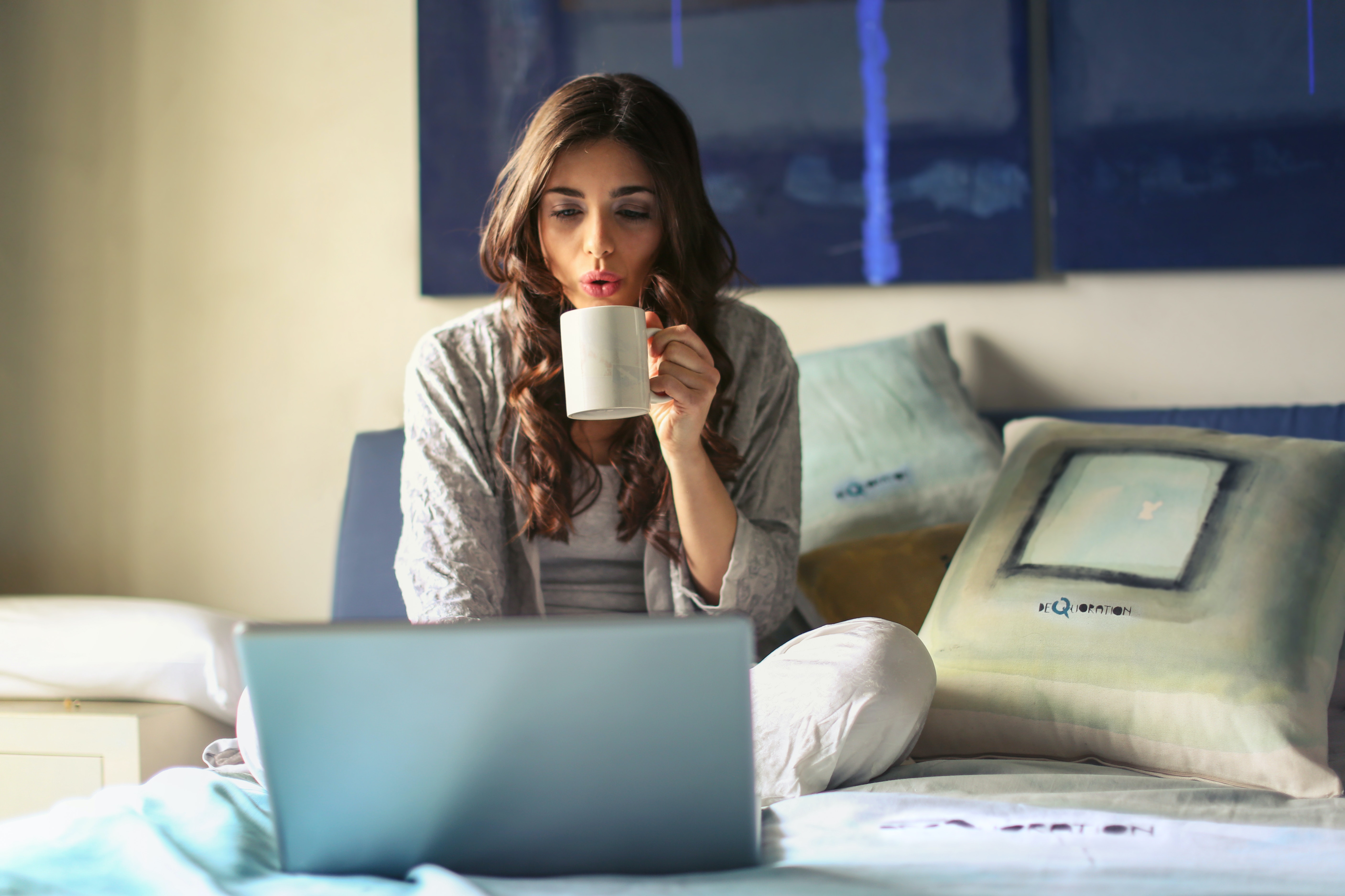 침대 위에서 커피를 마시며 인터넷 쇼핑을 하는 여성