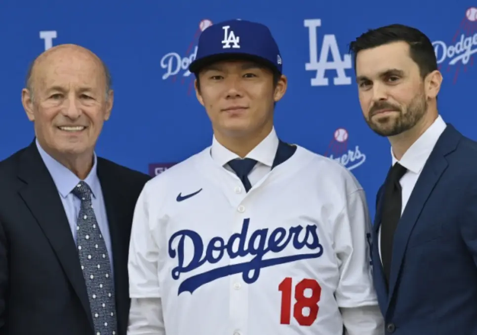 파란색 원단 위 흰글씨 LA dodgers 앞 흰유니폼 파란 야구모자를 쓴 야마모토 양쪽 양복을 입은 외국인이 웃고있는 모습