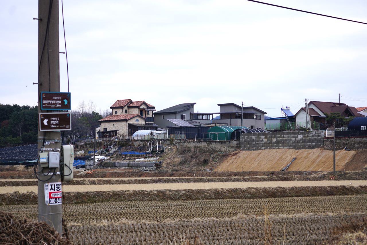 들판 위에 마을 풍경, 전원주택단지, 왼쪽 앞에 큰 전봇대에 붙은 양방향 이정표, 흐린 하늘,