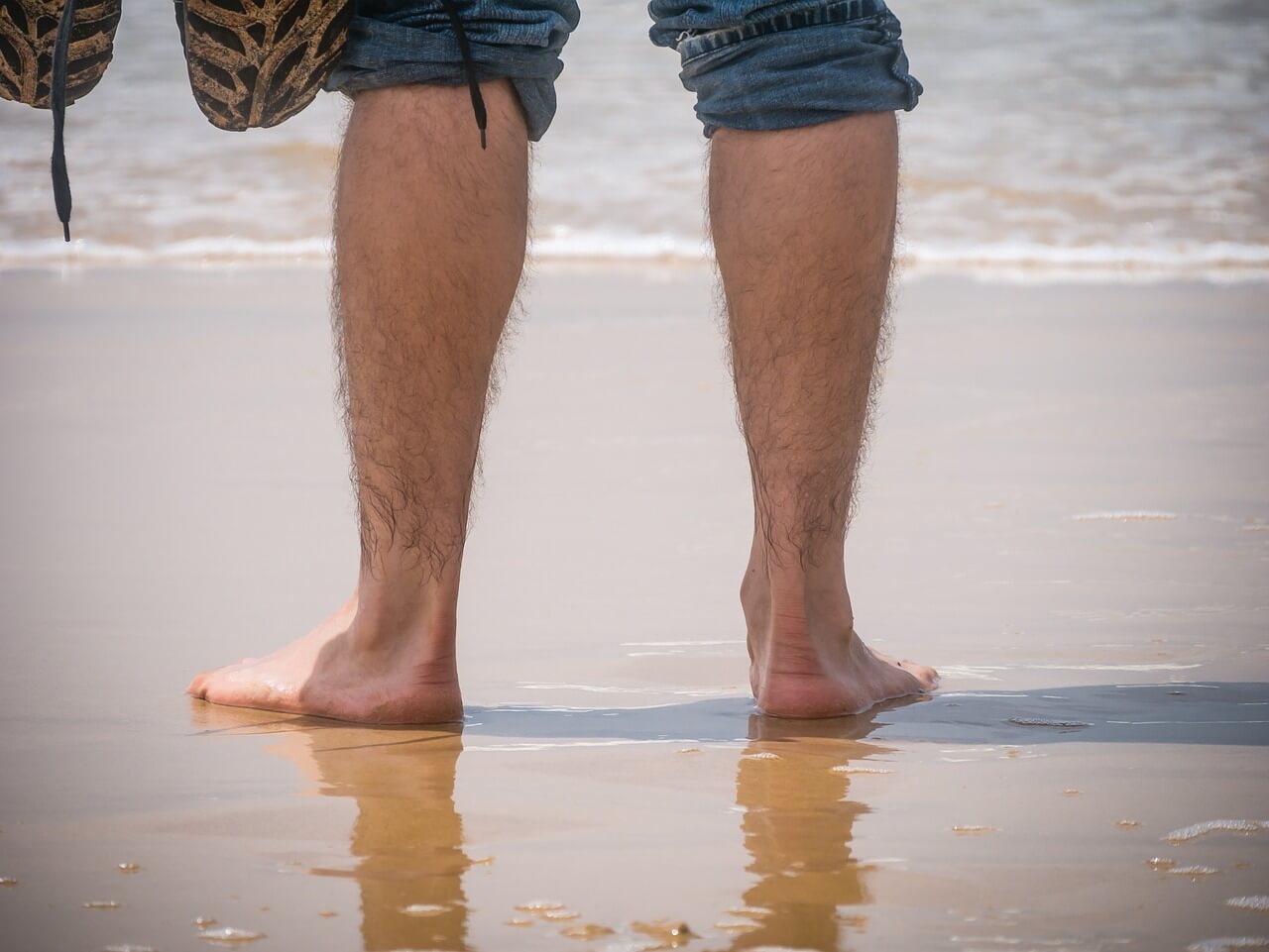 해변에서 바다를 보고 서있는 남자의 다리에 털이 수북한 사진