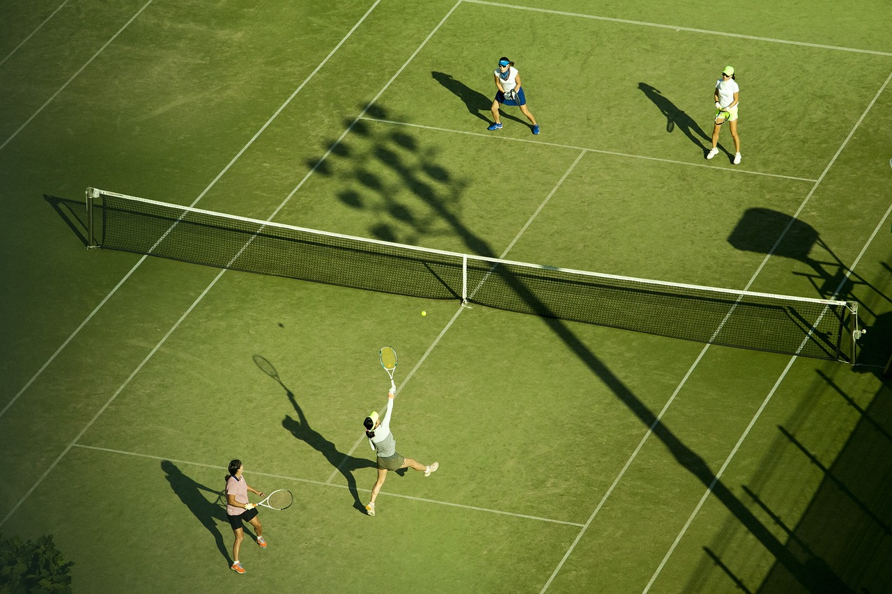 잔디가 가지런하게 깔려 있는 테니스장에서 2명씩 팀을 나눠서 테니스 복식을 치고 있는 사람들