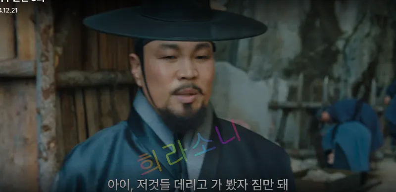 전통 모자를 쓴 지행수가 바깥에서 말을 하며 무언가를 지시하는 듯한 모습. 화면 하단 자막에는 &amp;quot;아이&amp;#44; 저것들 데리고 가 봤자 짐만 돼&amp;quot;라는 문구가 적혀 있다. 