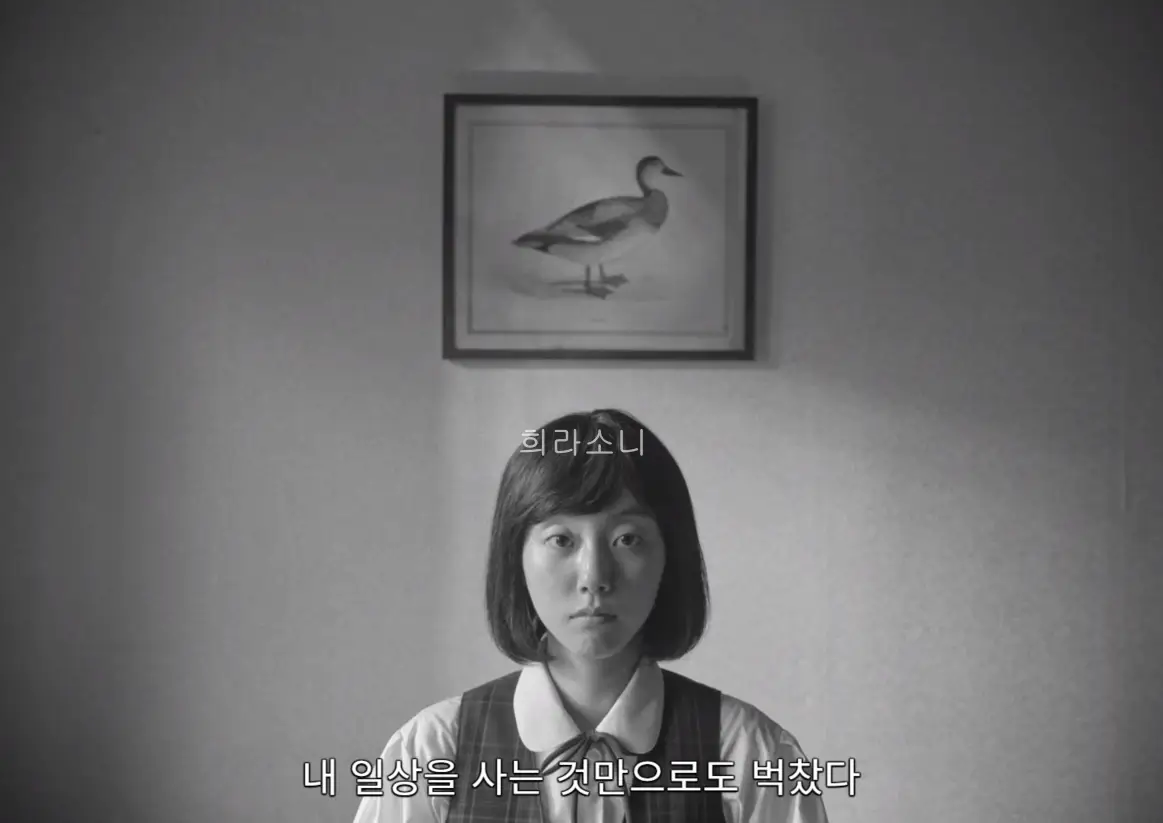 흑백 화면. 뒤에는 청동 오리 그림이 걸려 있고 앞에는 교복을 입은 무표정한 소녀가 앉아 있다. 자막 : 내 일상을 사는 것만으로도 벅찼다.