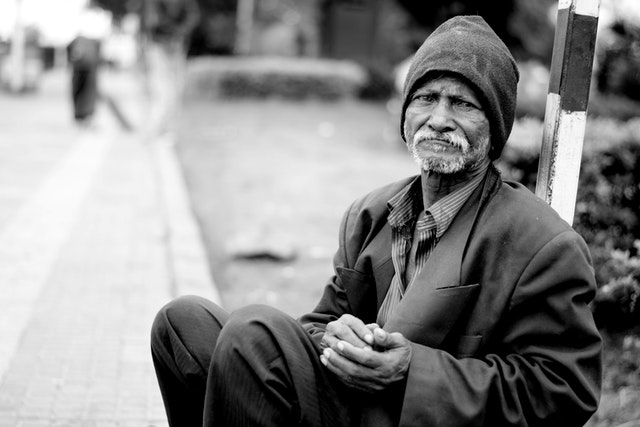 흑백사진속 한 노인이 길거리에 앉아있다.