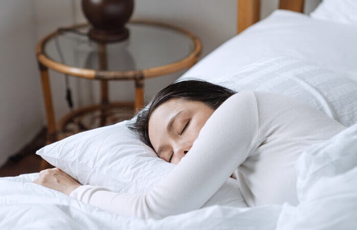 하얀색 티를 입은 여자가 하얀색 침구의 침대에서 자고 있는 모습 