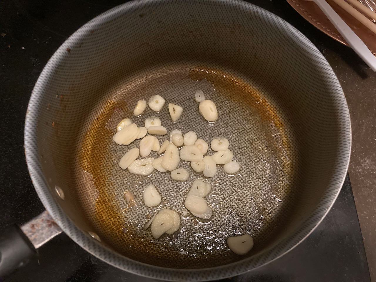 Sliced garlic and oil inside a cooking pot, which is on top of electric hot plate