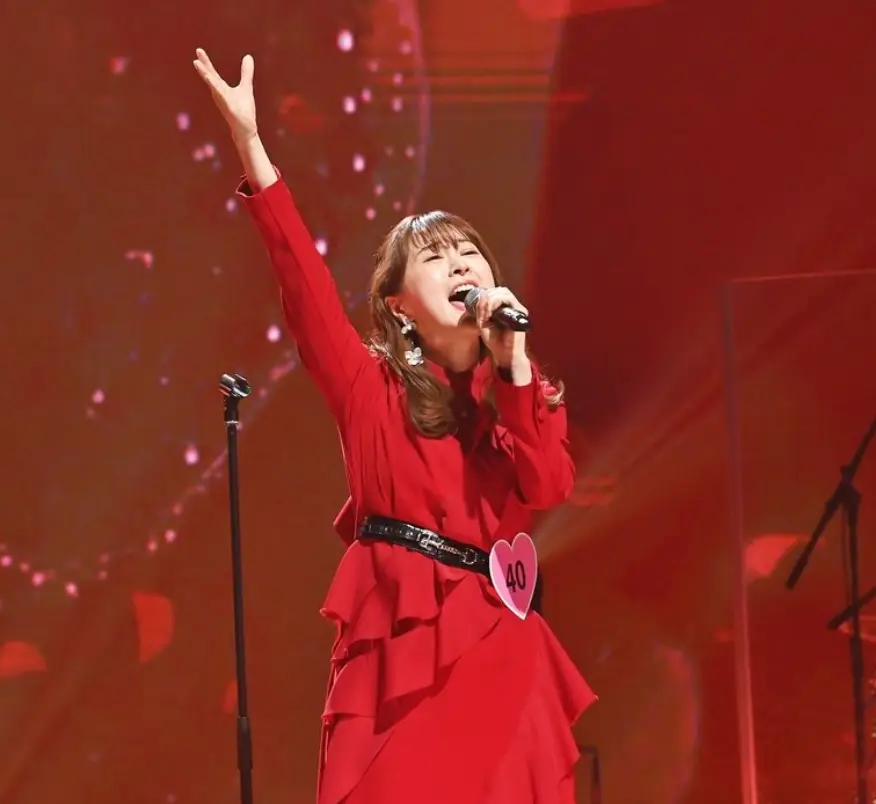 한일-붉은 무대배경 붉은 옷을 입고 왼손으로 마이크를 잡으채 열창을 하고 있는 나츠코