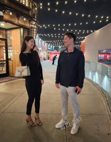 하림과 리키가 함께 약간 떨어져 서로를 바라보며 웃는 사진. 하림은 남색 셔츠에 회색 조거 팬츠를 입었고 하림은 상의&#44; 하의 모두 올 블랙에 검은 색 힐을 신었다.
